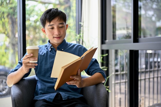 Happy Asian man enjoying with his coffee and reading a book in a coffee shop