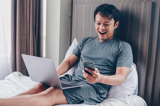 Happy Asian man is working with his laptop with video call in a bed Concept of freelancer successful lifestyle