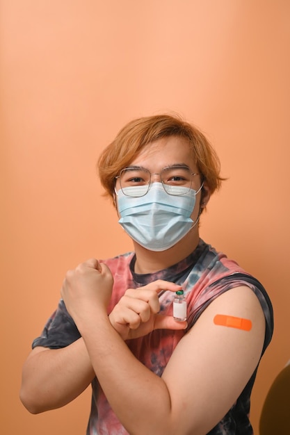 Happy Asian man showing his shoulder with bandage after getting vaccination