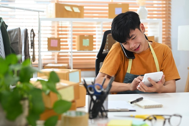 Happy asian man small business entrepreneur confirming orders or taking orders from customer on smart phone