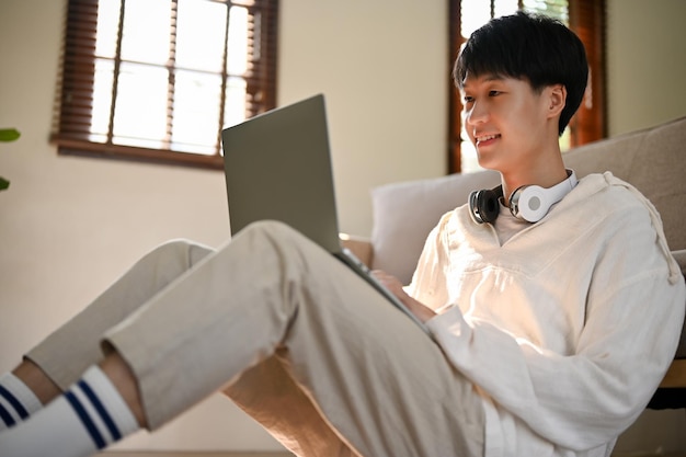 Happy Asian man using laptop while relaxing in his living room people an technology