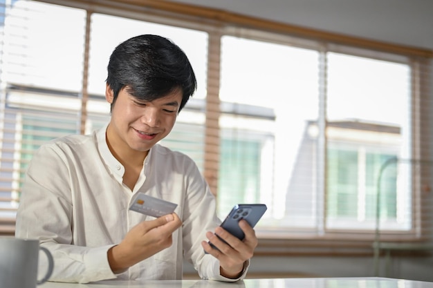 Happy Asian man using mobile banking application to transfer money or pay online bills