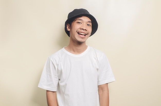 Happy asian man wearing bright white tshirt with black hat on isolated background