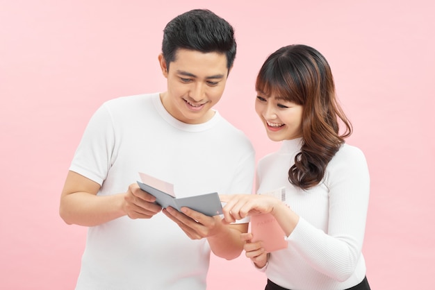 Happy asian man and woman holding passports and air tickets while looking at camera isolated on pink