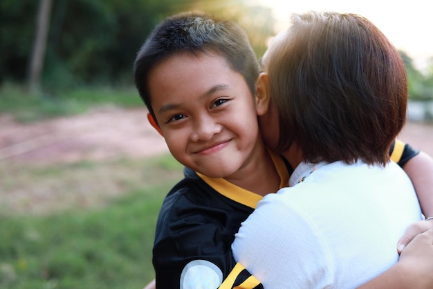 Happy Asian mother hold in arms hug smiling cute little son, Enjoy a family weekend in the backyard together at sunset. Caring mom embrace boy child, show love, have tender sweet close moment.