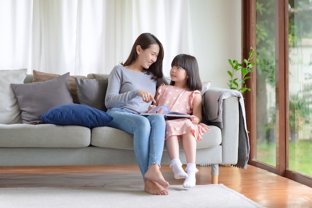 Happy asian mother teaching her cute kid daughter to studying in living room at home