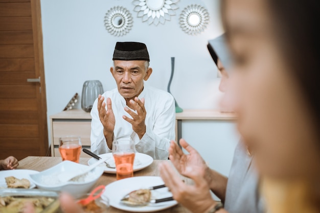 Happy asian muslim family praying before having their iftar meal during ramadan fasting