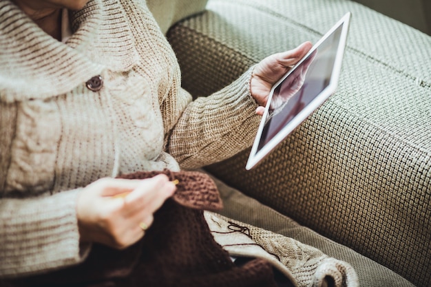 Happy asian old woman knit brown scarf crochet and tablet on sofa in living room at home