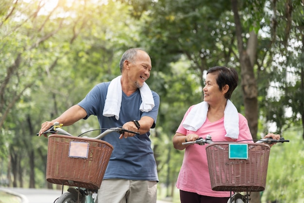 Happy Asian Senior couple in blue and pink shirt laughing while riding the bicycles.