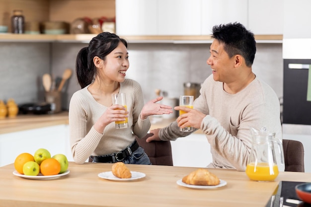 Happy asian spouses having fun while eating at kitchen