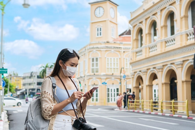 Happy Asian traveler woman looking a map on mobile phone while walking at old town Phuket Thailand Travel alone Summer and holiday concept