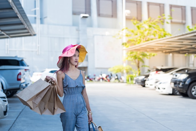 Happy asian woman in fashion casual dress with shopping bags and walking in parking lot.