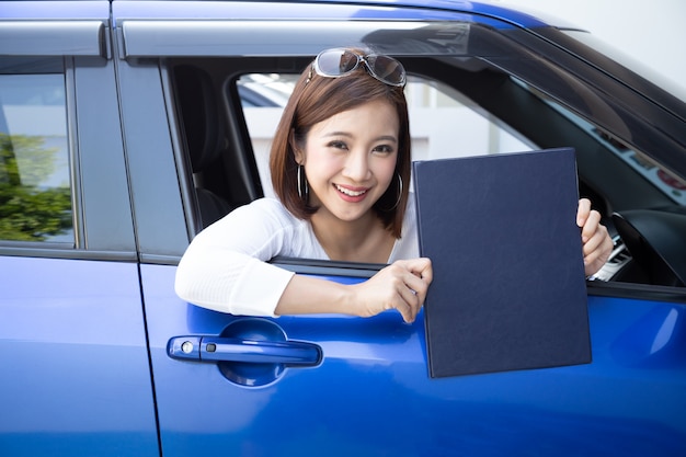 Happy Asian woman holding car insurance document book and sitting in car, Safety vehicle and protection client person concept