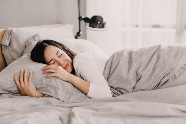 Happy asian woman is resting on gentle pillow on bed