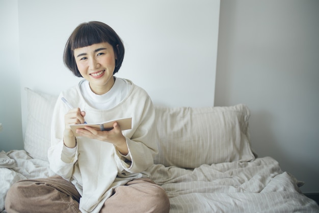 Happy Asian woman is writing at bedroom. She work from home.