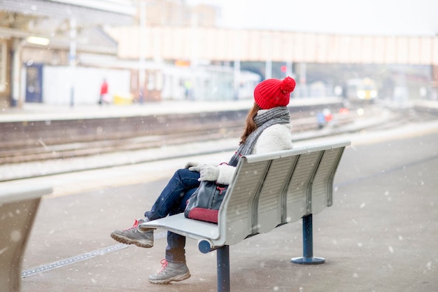 Happy asian woman in red hat white coat sitting at the station and waiting for train