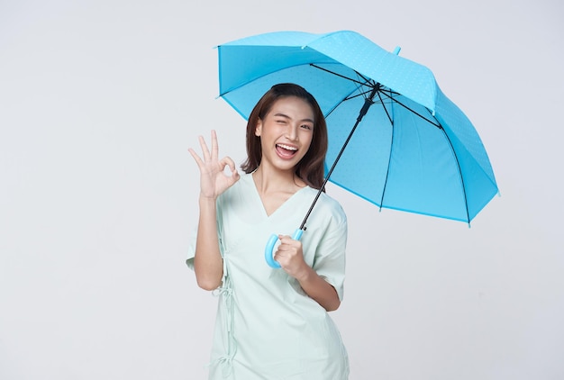 Happy Asian woman standing holding blue umbrella and showing ok sign isolated on white background