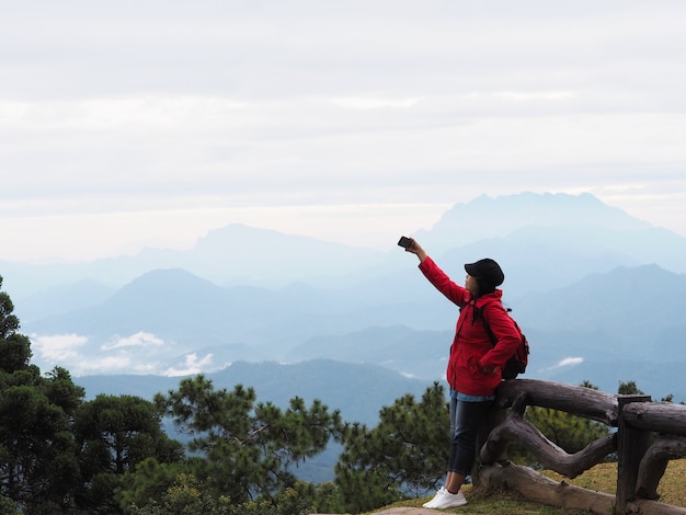 Happy Asian woman tourist taking photograph over mountain view with fog background