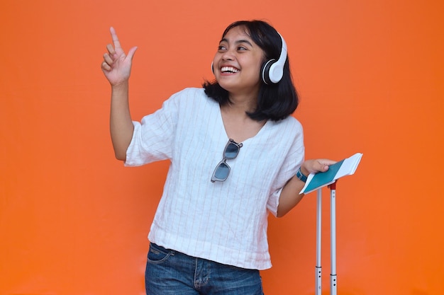 Happy Asian woman tourist using headphone while pointing finger to copy space