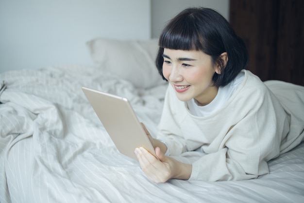 Happy Asian woman using taplet for work at bedroom.