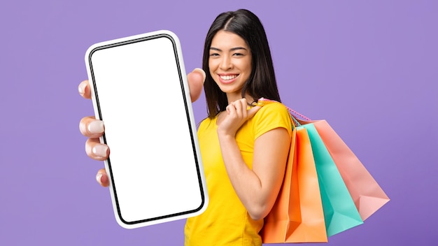 Happy Asian Woman With Shopper Bags Demonstrating Blank Smartphone Screen