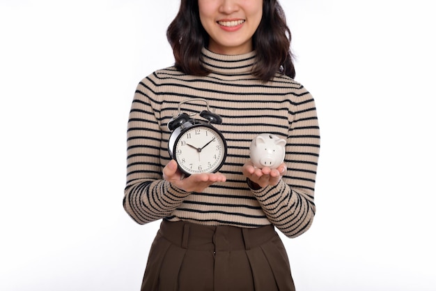 Happy Asian woman with sweater shirt holding alarm clock and piggy bank isolated on white background