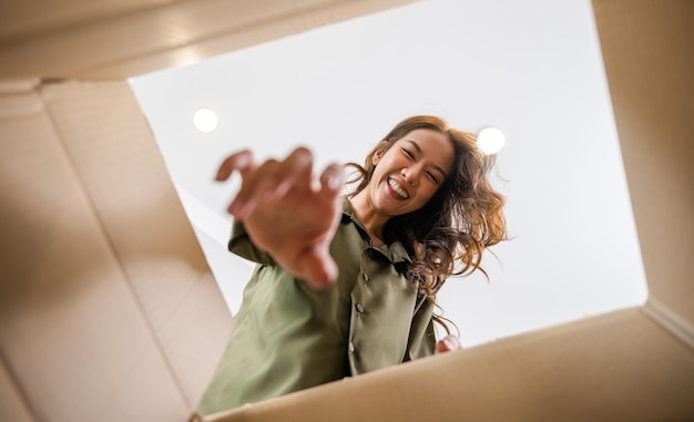 Happy Asian young woman opening carton box from internet store order shopping online at home, Smiling female surprised unpacking christmas gift big box and looking inside, inside bottom view