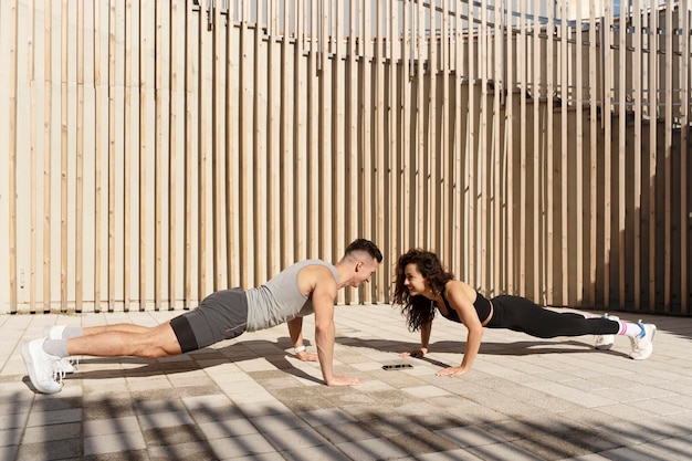 Happy athlete couple standing at plank pose together and making push ups