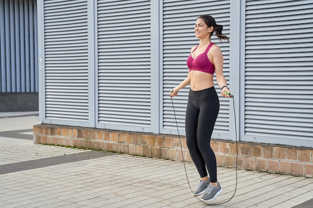 Happy athletic woman doing cardio workout with a skipping rope outdoors in the morning. Sport concept. Copy space