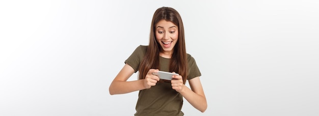 Happy attractive brunette girl joying win in video game on smartphone isolated over grey background