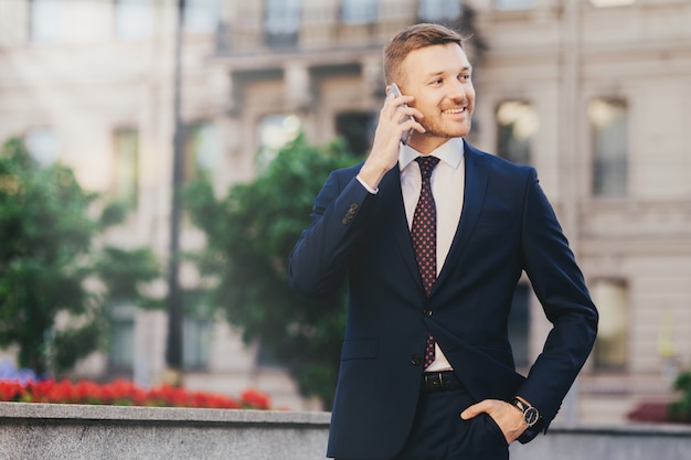 Happy attractive male financier in elegant wear, using modern smartphone