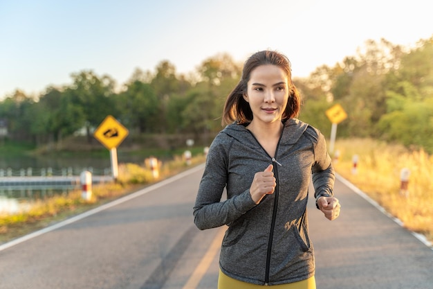 Happy attractive young woman wearing her warm up jacket while running at a local park during her early morning exercise routine warm sunrise