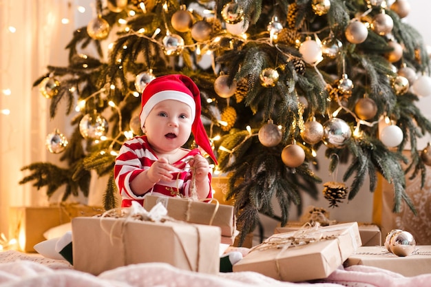 Happy baby 1 year old open Christmas present box sitting on floor under Christmas tree closeup Winter season Childhood