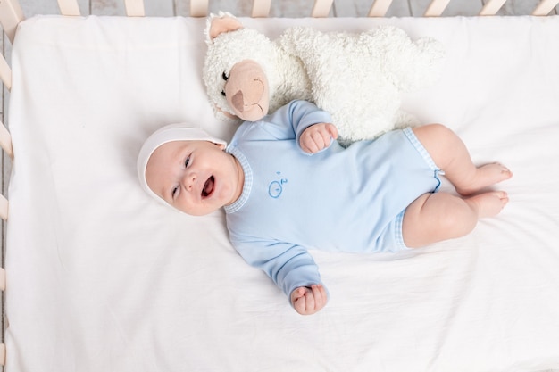 Happy baby boy in crib with teddy bear toy, children and birth concept