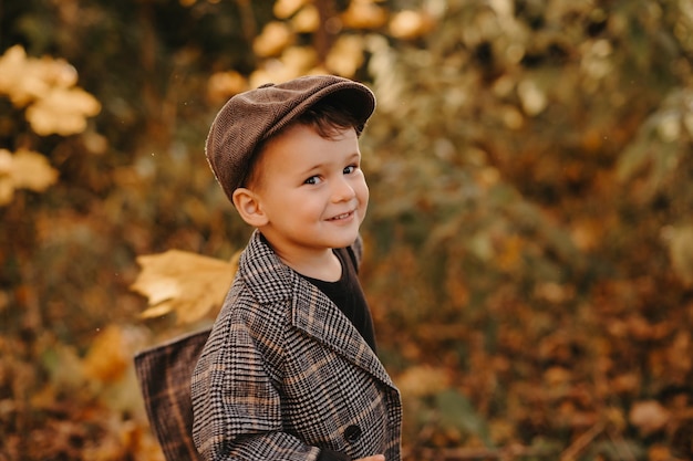 A happy baby boy is playing with yellow leaves in the golden autumn season in the park