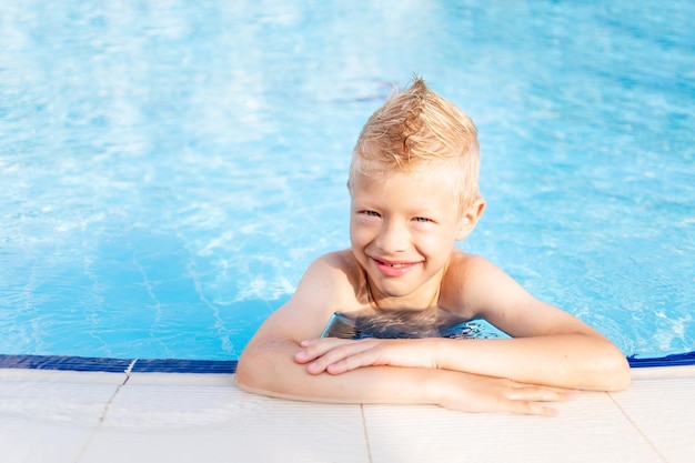 Happy baby boy in the pool with blue water bathing and smiling the concept of summer vacation and travel