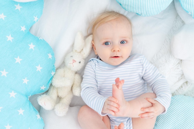 Happy baby boy six months old lying on the bed with a stuffed toy bunny cute blonde baby