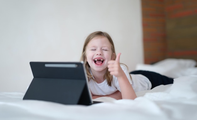 Happy baby girl holding thumbs up with tablet