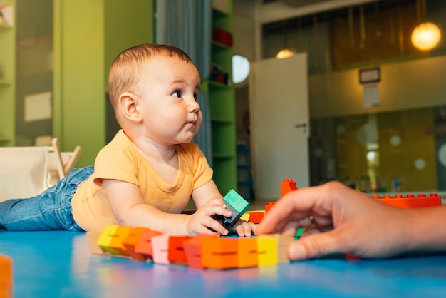 Happy baby playing with toy blocks in the kindergarten.