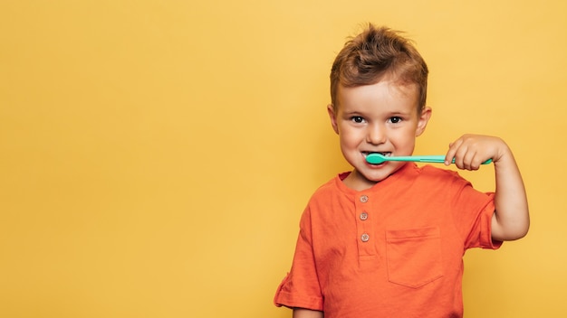 Happy baby toddler boy brushing his teeth with a toothbrush on a yellow background. Health care, oral hygiene. A place for your text.