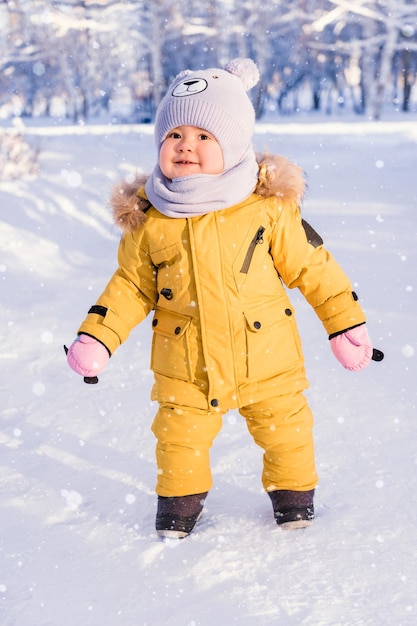 A happy baby in winter clothes enjoys the snow while walking in the winter park Close up