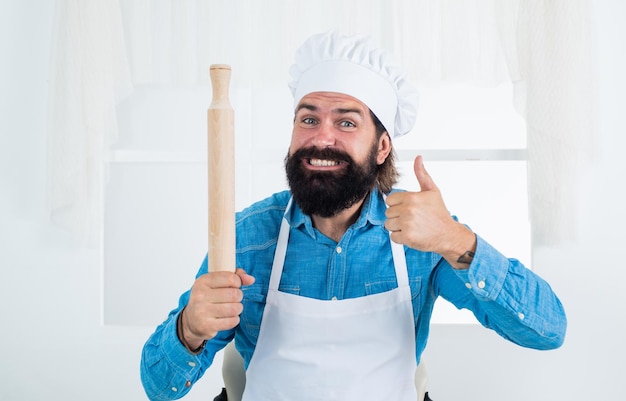 Happy baking concept of housekeeping mature bearded man wear chef hat holding rolling pin best quality male cook preparing food in kitchen brutal hipster in apron cooking meal time for eating