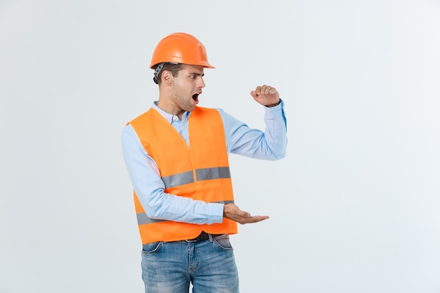 Happy beard engineer holding hand on side and explaining something, guy wearing caro shirt and jeans with yellow vest and orange helmet, isolated on white background.