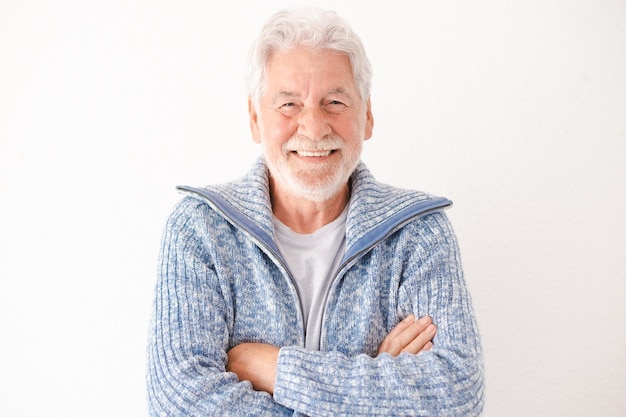 Happy bearded elderly male in casual clothes smiling and looking at camera while standing with crossed arms on white background