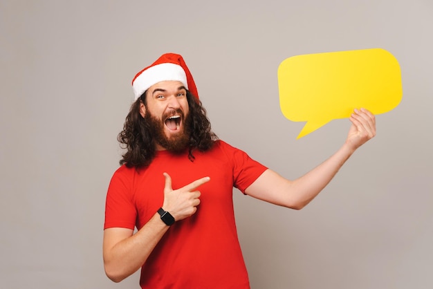 Happy bearded man is holding and pointing at yellow bubble speech for holidays