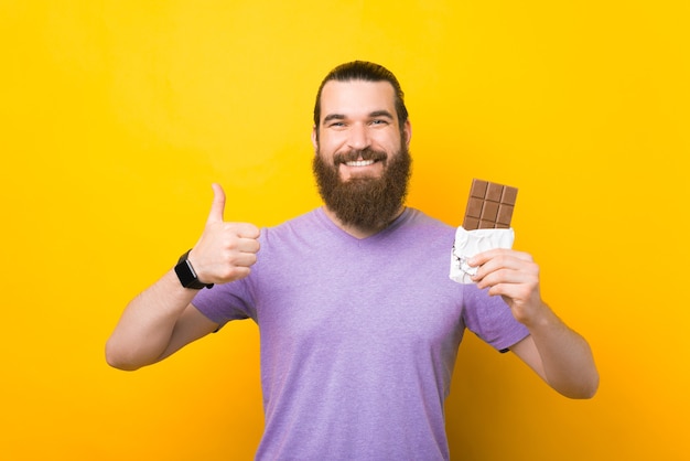 Happy bearded man is showing like gesture and a whole chocolate bar.