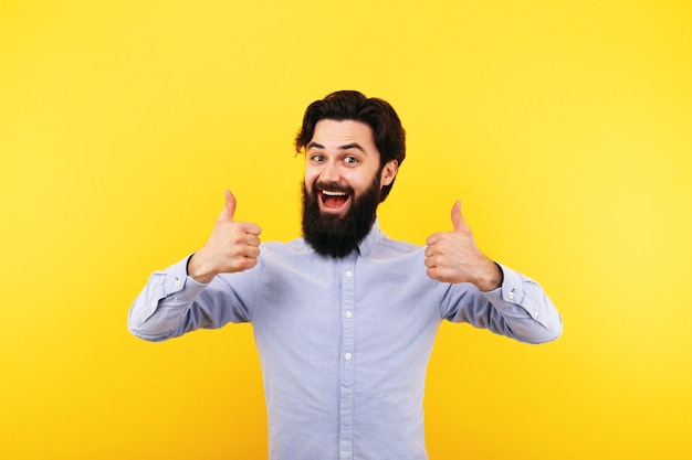 Happy bearded man showing thumb up and smiling over yellow wall