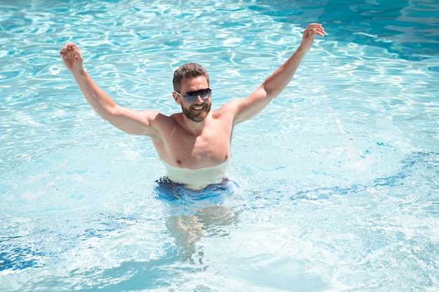 Happy bearded man in sunglasses having fun in swimming pool water on summer holidays, summer vacation.