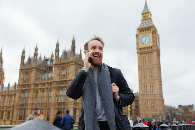 Happy bearded man talking on the phone while standing on the background of the Big Ben tower