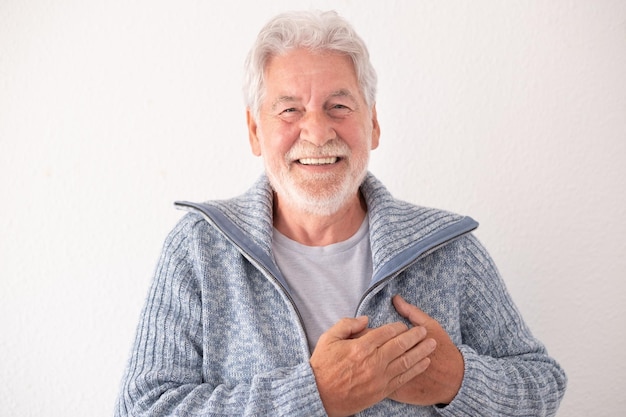 Happy bearded senior man in casual clothes smiling and looking at the camera while crossing his hands over his heart concept of thanksgiving and love